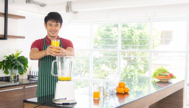 Akıllı ve yakışıklı Asyalı adam, tavan arası mutfağında sağlıklı yemek ve taze organik portakal suyu hazırlıyor..