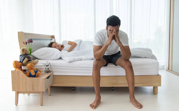 Aile sorunu ve ilişki kavramı. Genç Asyalı üzgün adam yatakta oturuyor. Kadın arka planda..