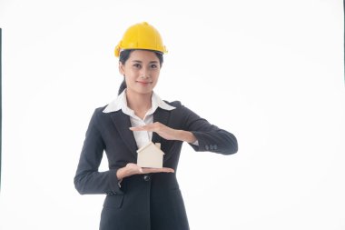 Genç mühendis kadın siyah takım elbise ve sarı kaskla izole edilmiş beyaz arka planda küçük ev modelini tutuyor..