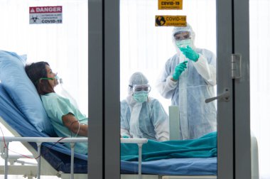 Koruyucu giysili doktorlar hastanedeki karantina odasında CORONA VISRUS veya COVID-19 ile enfekte olan hastanın kan basıncını ölçer ve ölçer..