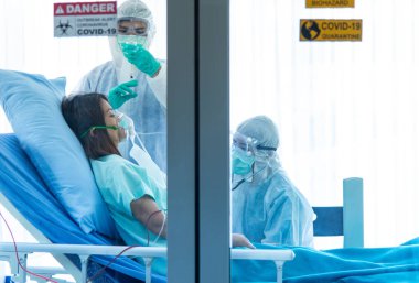 Koruyucu giysili doktorlar hastanedeki karantina odasında CORONA VISRUS veya COVID-19 ile enfekte olan hastanın kan basıncını ölçer ve ölçer..