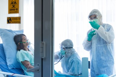 Koruyucu giysili doktorlar hastanedeki karantina odasında CORONA VISRUS veya COVID-19 ile enfekte olan hastanın kan basıncını ölçer ve ölçer..