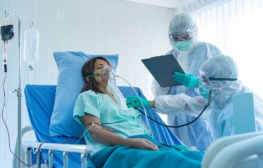Koruyucu giysili doktorlar hastanedeki karantina odasında CORONA VISRUS veya COVID-19 ile enfekte olan hastanın kan basıncını ölçer ve ölçer..