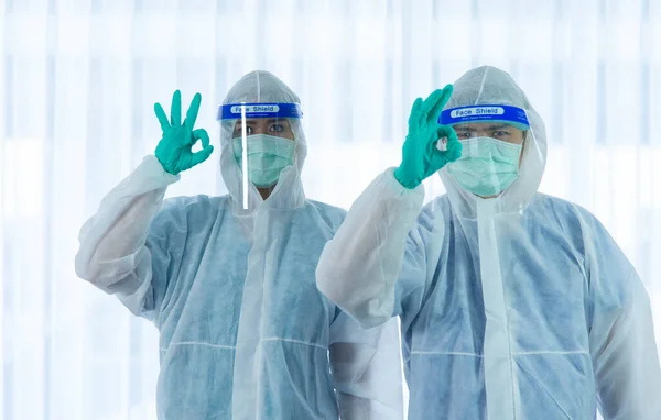 Two medical staffs with PPE suit and facial mask standing and hand up for fighting beside aging woman patient infected with CORONA VISRUS or COVID-19 bedroom in quarantine room at the hospital.