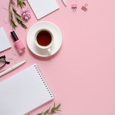 Pembe arka planda not defteri, kalem, kahve fincanı ve diğer aksesuarları olan işyeri