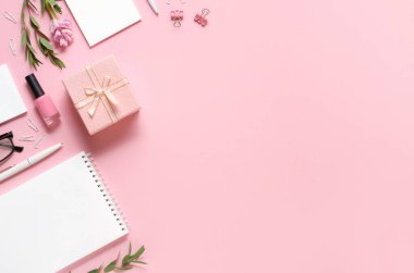 Pembe arka planda not defteri, kalem, hediye ve diğer aksesuarlara sahip işyeri