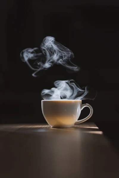 Hot water in white coffee cup on wooden table with smoke and nature light on black background