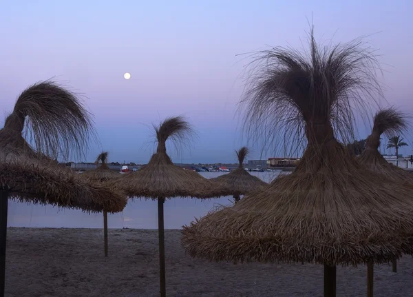 Straw parasols and full moon — Stock Photo, Image