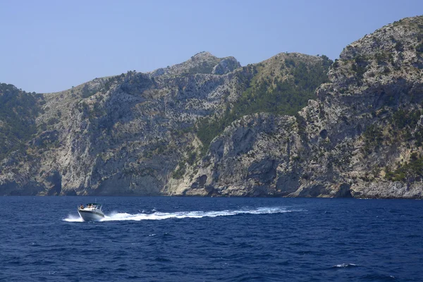 Small boat, blue ocean and rocky seashore — Stock Photo, Image