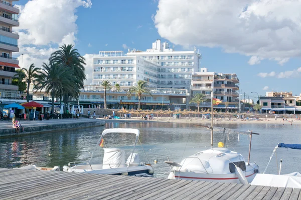 Small boats by the Cala Estancia jetty and hotels along the street and boardwalk — Stock Photo, Image