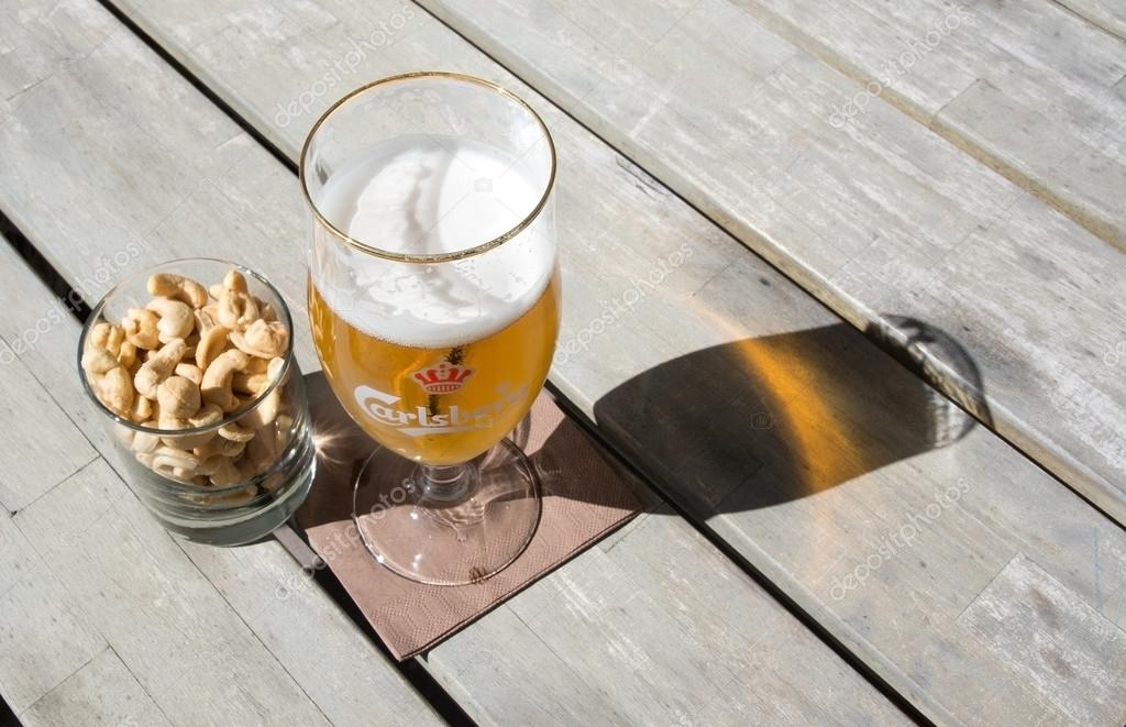 FALKENBERG, SWEDEN - JUNE 5, 2015: Two beers in Carlsberg logo glasses on rustic wooden table with cashew nuts outdoors in sunshine on June 5, 2015 in Falkenberg, Sweden.