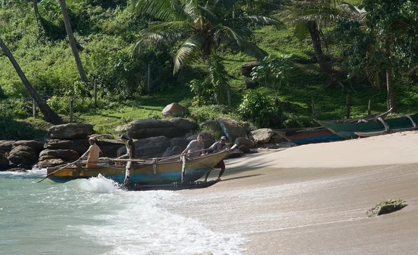 Four men drag their small wooden boat up onto the sandy beach after a fishing tour — Stock Photo, Image