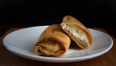 Beyaz tabakta süzme peynirle doldurulmuş krepler.