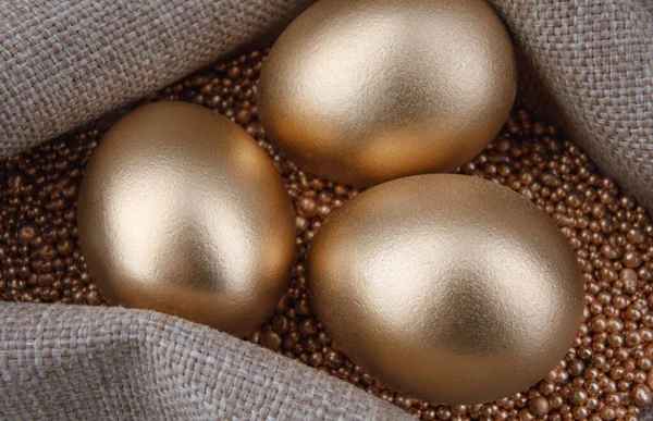 Three golden eggs on gold sand.