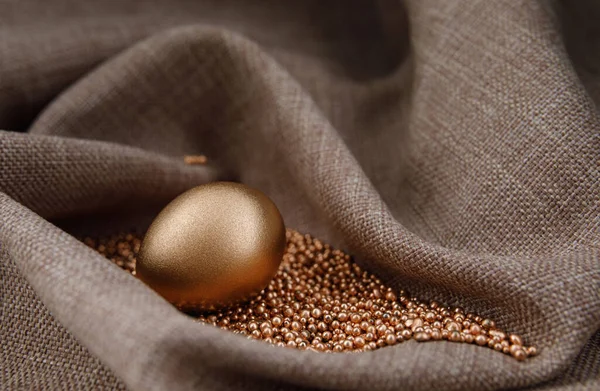 Golden egg on gold sand in waves of cloth.