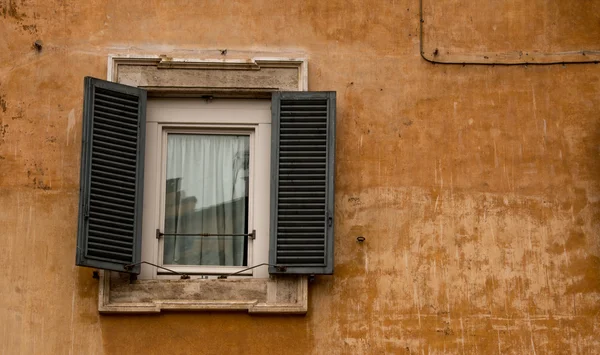 Uma janela romana, com persianas, situada em uma parede ocre colorida — Fotografia de Stock