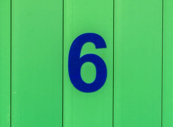 The number six, blue, set against bright green wood — Stock Photo, Image