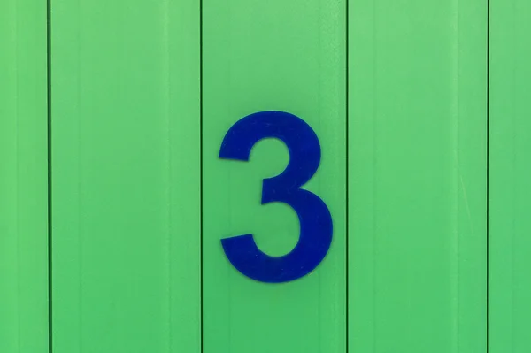 Het nummer drie, blauw, ingesteld tegen helder groen hout — Stockfoto
