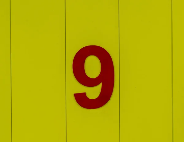 Number nine, red, set against bright yellow wood — Stock Photo, Image