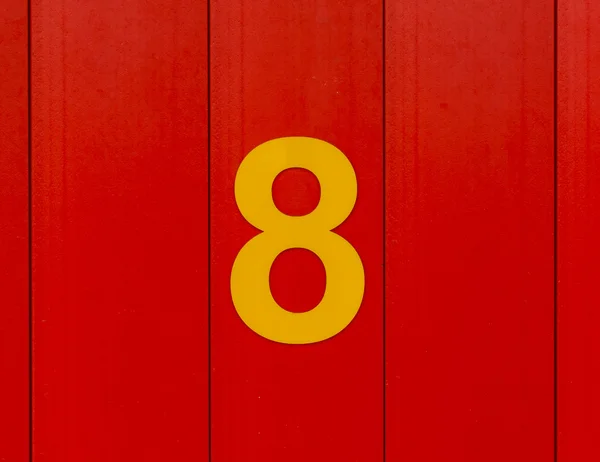 Het nummer acht, geel, ingesteld tegen heldere rode hout — Stockfoto