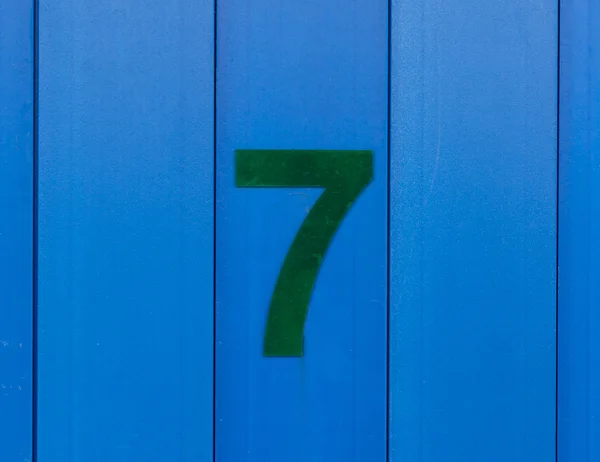 Número sete, verde, contra a madeira azul brilhante Imagem De Stock