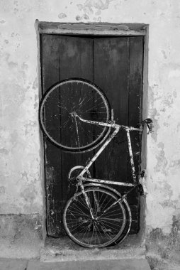Paslı beyaz bisiklet Trapani Sicilya 'daki Favignana adasında mavi ahşap bir kapıyı kapatır.