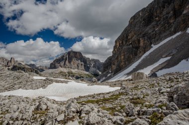 İtalya 'nın Cortina d' Ampezzo Belluno bölgesindeki Falzarego geçidinde Dolomitlerin yeşil çayırlarında kar ve pembe kayalarla bahar manzarası.