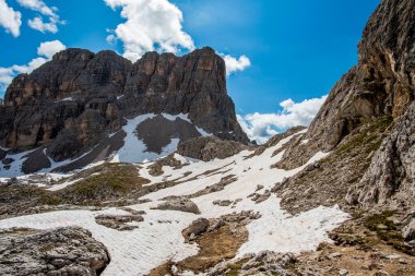 İtalya 'nın Cortina d' Ampezzo Belluno bölgesindeki Falzarego geçidinde Dolomitlerin yeşil çayırlarında kar ve pembe kayalarla bahar manzarası.