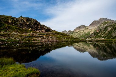 İtalya, Trentino 'daki Lagorai dağlarında sakin bir alp gölü. Kayalık yamaçlar ve tepeler durgun suya yansıyor mavi gökyüzünün altında, huzurlu dağ yabanı