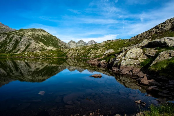 İtalya, Trentino 'daki Lagorai dağlarında temiz alp gölü. Parlak mavi gökyüzü ve kayalık tepeler sakin suda yansıtılır, el değmemiş doğal dağ manzarası.
