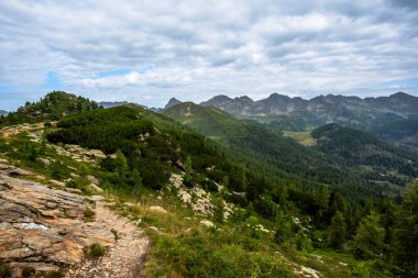 Kuzey İtalya 'nın Lagorai dağlarında bulutlu bir gökyüzünün altında kayalık yamaçları, yoğun ormanları ve sivri dağ tepeleri olan geniş bir dağlık vadi..