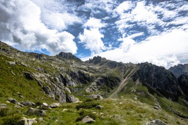 İtalya, Pieve Tesino yakınlarındaki Lagorai dağlarının kayalık tepeleri, engebeli uçurumlar, yeşil yamaçlar ve parlak yaz bulutları..