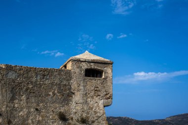 Korsika, Fransa 'da açık mavi gökyüzüne karşı gözetleme kulesi olan antik taş kale duvarı. Tarihi askeri mimari, kaba doku, minimum bileşim ve güçlü Akdeniz atmosferi.