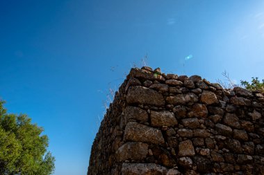 Korsika kırsalında, parlak mavi gökyüzü altında antik bir taş kalıntısının köşesinde, Akdeniz kırsal mimarisi, sakin bir doğal ortamda erozyon, doku ve zamansız Avrupa mirasını gösteriyor..