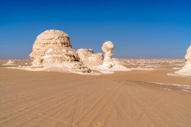Mısır 'ın Giza yakınlarındaki Beyaz Çölde kumlu zemine dağılmış aşınmış kireçtaşı oluşumlarının geniş görüşü jeolojik dokuları ve kurak iklimi vurguluyor..
