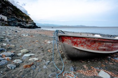 Weathered small boat resting on a rocky shoreline beside the sea. Coastal landscape suitable for travel, tourism, and marine concepts with copy space and calm atmosphere.