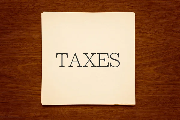 Papieren kaarten met woord "Belastingen" op houten achtergrond in sepia — Stockfoto