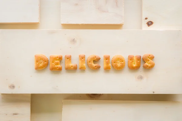 Parola DELICIOSO Alfabeto Biscotti su fondo legno — Foto Stock