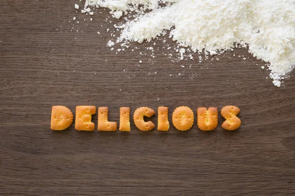 Parola DELICIOSO Alfabeto Biscotti sulla scrivania in legno — Foto Stock