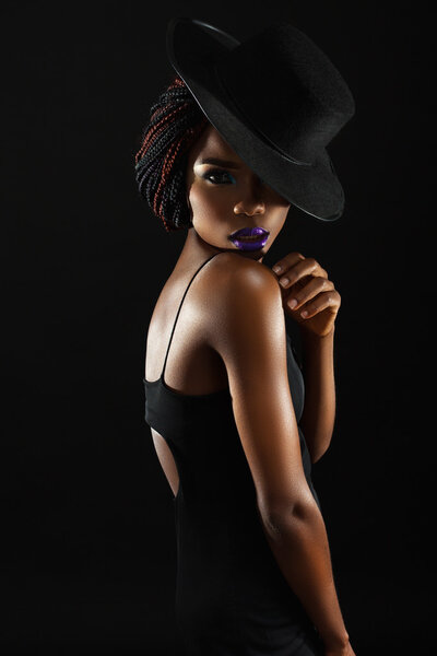 Dark skinned woman on a black background with a fashionable hat on his head
