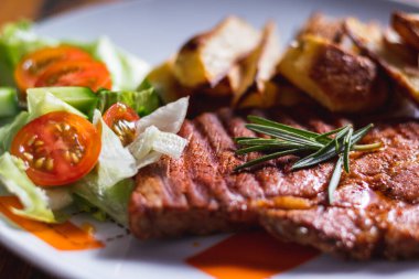 Kızarmış domuz eti, fırında patates ve salata. Yemek tabakta servis edilir. Lezzetli ızgara et. Ahşap arka planda beyaz tabakta kızarmış domuz eti..