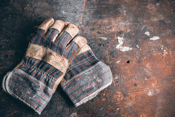 A pair of protection gloves. Old leather gloves on wooden table. Working gloves on wood workbench. A dirty and well-worn pair leather work gloves.