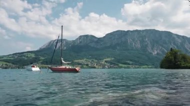 Yukarı Avusturya 'daki Attersee Gölü' nün turkuaz sularında yüzen bir yelkenlinin huzurlu manzarası güneşli bir yaz gününde yeşil tepeler ve dağlarla çevrili..