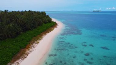 Kumlu bir sahil boyunca alçak irtifa drone uçuşu. Solda Sikandang Adası, sağda açık mavi okyanus. Kamera hafifçe aşağı eğilmiş..