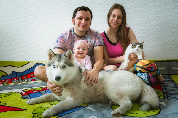 Feliz joven familia sentada en el suelo con gato y perro mascota en casa —  Fotos de Stock