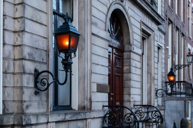 Tarihi Amsterdam cephesindeki iki retro fenerin ılık turuncu parıltısı. Alacakaranlıkta klasik Hollanda mimarisi. Sıcak, klasik bir atmosferi var.