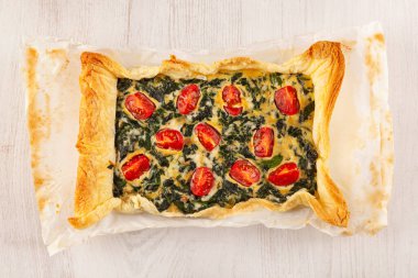 Vejetaryen ıspanaklı turta ya da peynirli kiş ve yukarıdan beyaz ahşap arka planda domates.. 