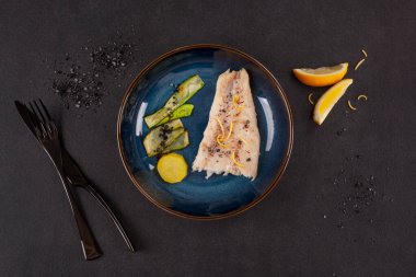 Güzel yemek. Kabak dilimli ızgara balık filetosu, patates ve lav tuzu koyu arkaplanda..