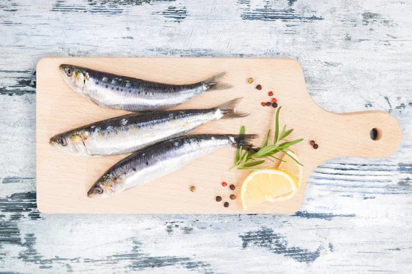 Peixe de anchova fresco na placa de cozinha de madeira . — Fotografia de Stock