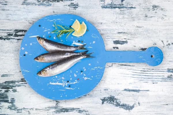 白色和蓝色的木制厨具板新鲜鳀鱼. — 图库照片